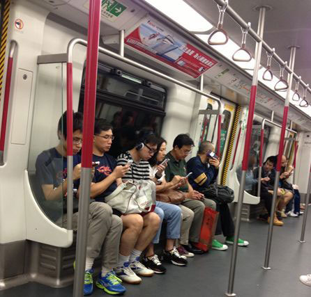 A row of passengers on a train. Each passenger uses a mobile device.