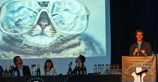 Speaker at a podium. The screen shows a photo of a cat in glasses.