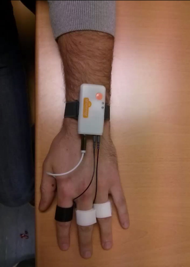 A hand with sensors worn like bands around three fingers and a small electronic device worn on the wrist.
