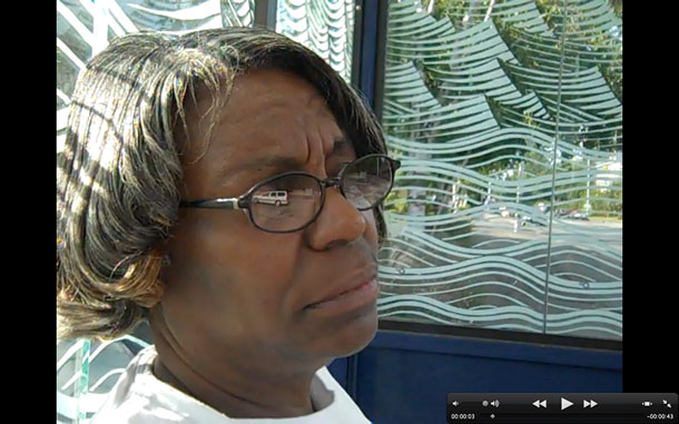 A screen capture of a video where a woman waits at a bus stop.