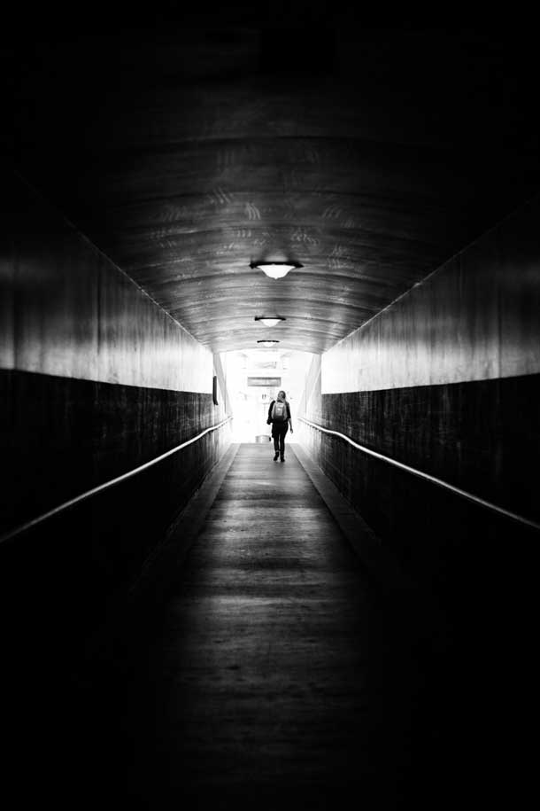 A figure walks down a dark hallway towards a light.
