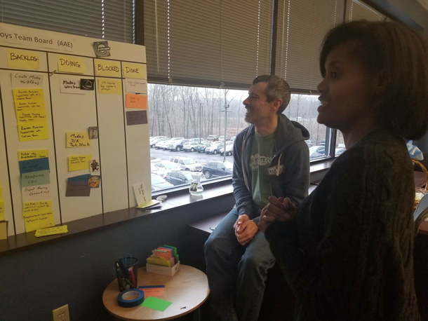 A man and a woman stand at the status board discussing the work.