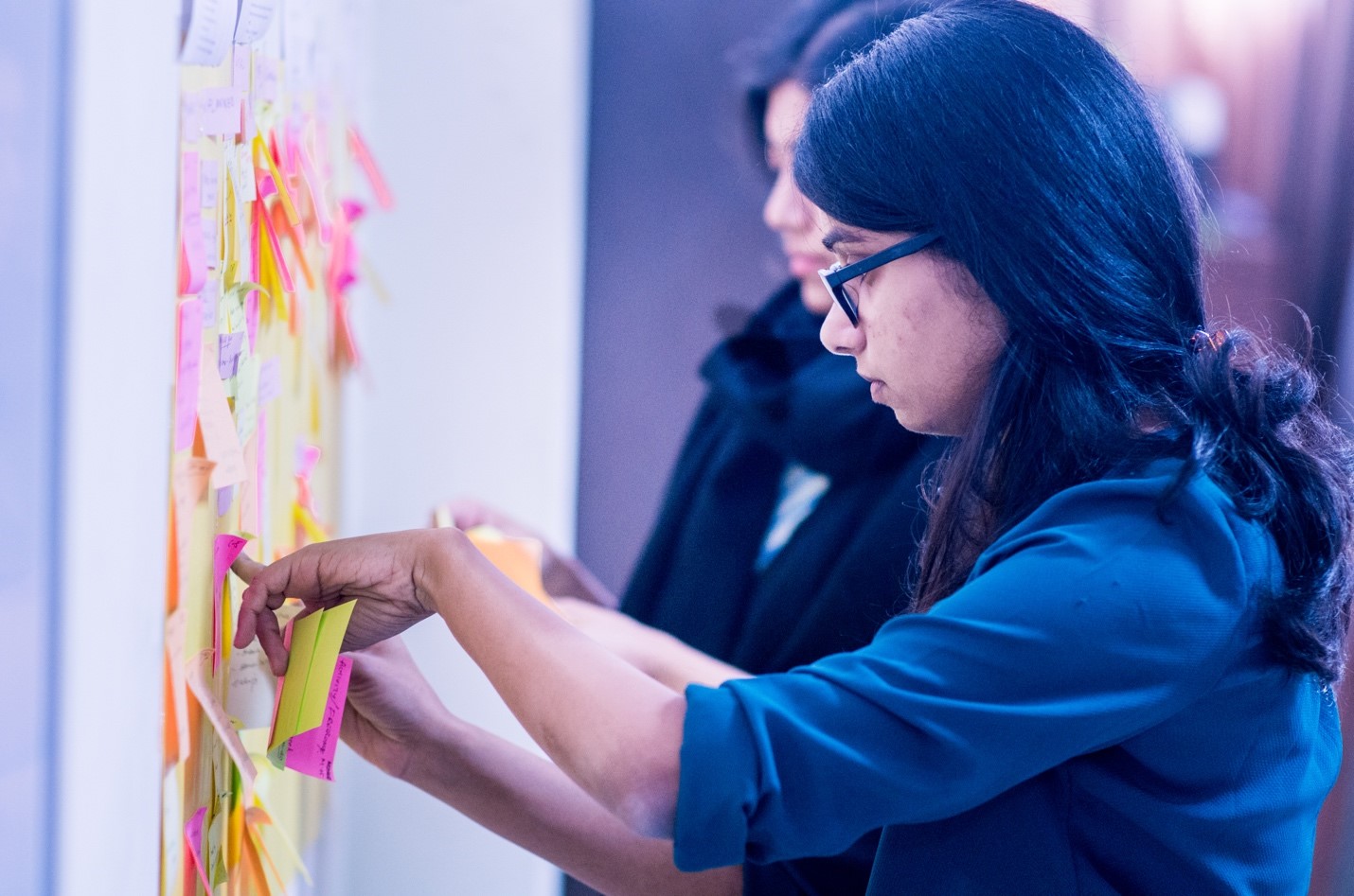 A photograph of two women sorting sticky notes on a wall.